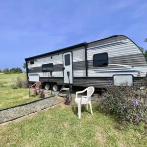 A white chair sitting in the grass near a trailer.