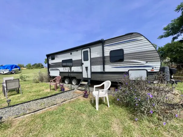 A white chair sitting in the grass near a trailer.