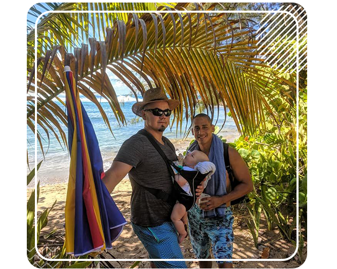 A man and woman holding a baby under a palm tree.