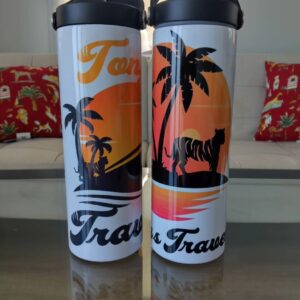 Two travel mugs sitting on a table next to pillows.