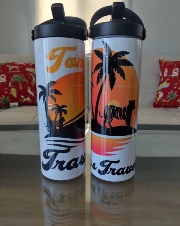 Two travel mugs sitting on a table next to pillows.